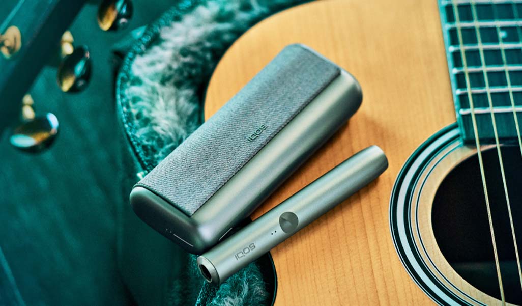 ILUMA Prime device and charging case placed on an IQOS users acoustic guitar.