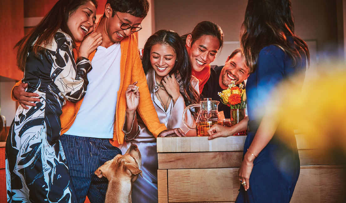 A group of friends relax on a sofa; one holding an IQOS device.