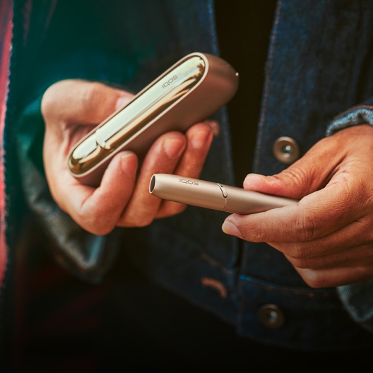Close up of a male hand holding a gold IQOS ILUMA device and  case.