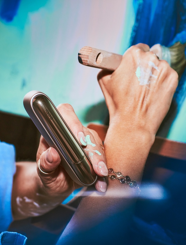 An artist's hand holding an IQOS ILUMA case as she paints.