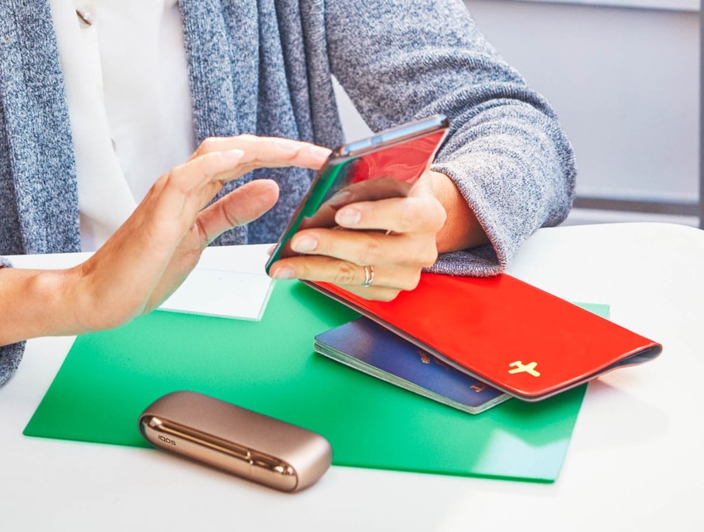 Girl checking her phone at a bar with a IQOS device on the table and the luggage next to her