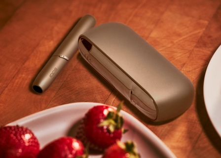 Brilliant gold IQOS 3 DUO holder with HEETS stick and charger next to a plate of strawberries