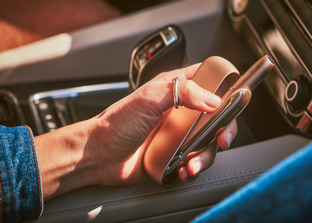 Woman's hand holding a brilliant gold IQOS 3 DUO holder and charger in a car