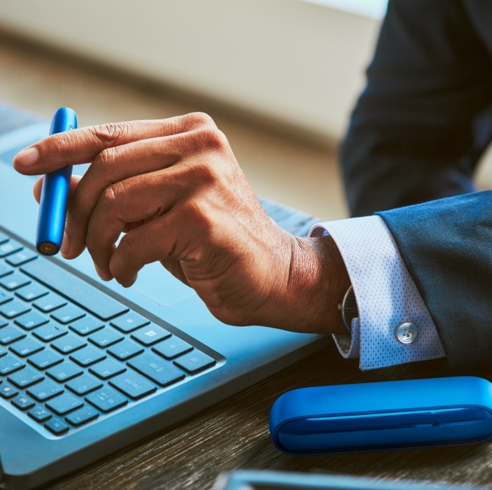 Stellar blue IQOS 3 DUO holder and charger in businessman's hand with HEETS stick inserted