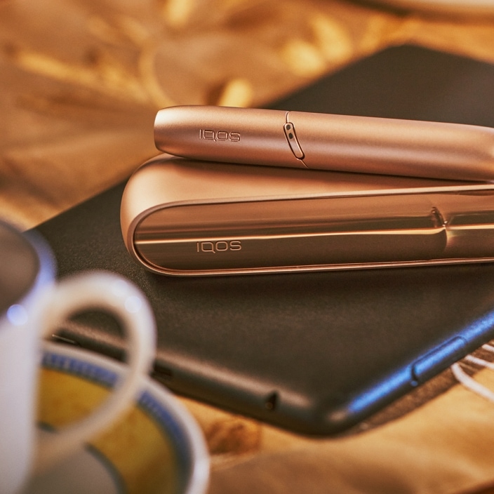 Brilliant gold IQOS 3 DUO with HEETS stick on top of charger