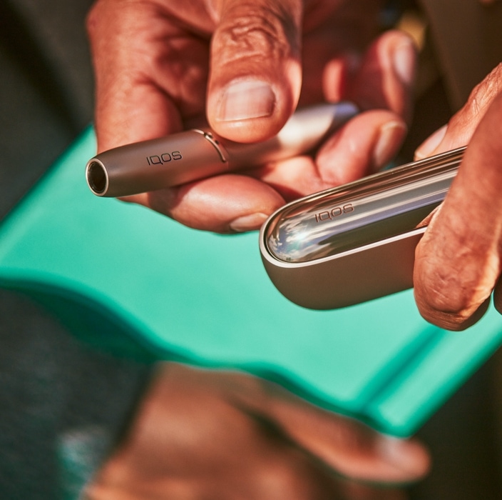 Brilliant gold IQOS 3 DUO with HEETS stick and charger next to binoculars on a blue blanket