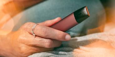 Two people talking at a table bar, one smokes IQOS and the other uses his phone